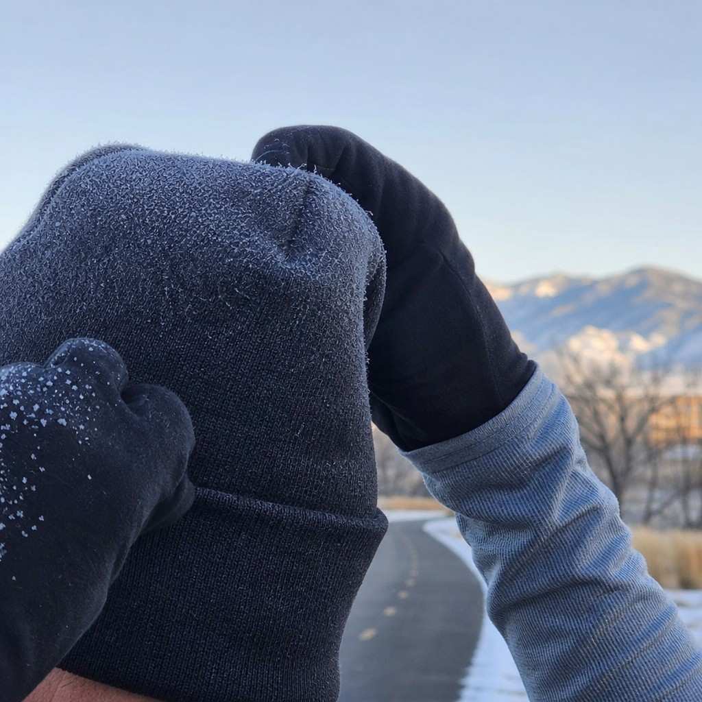 Close-up of a runner's gloved hands and a knit hat with frost on the fabric on a freezing morning