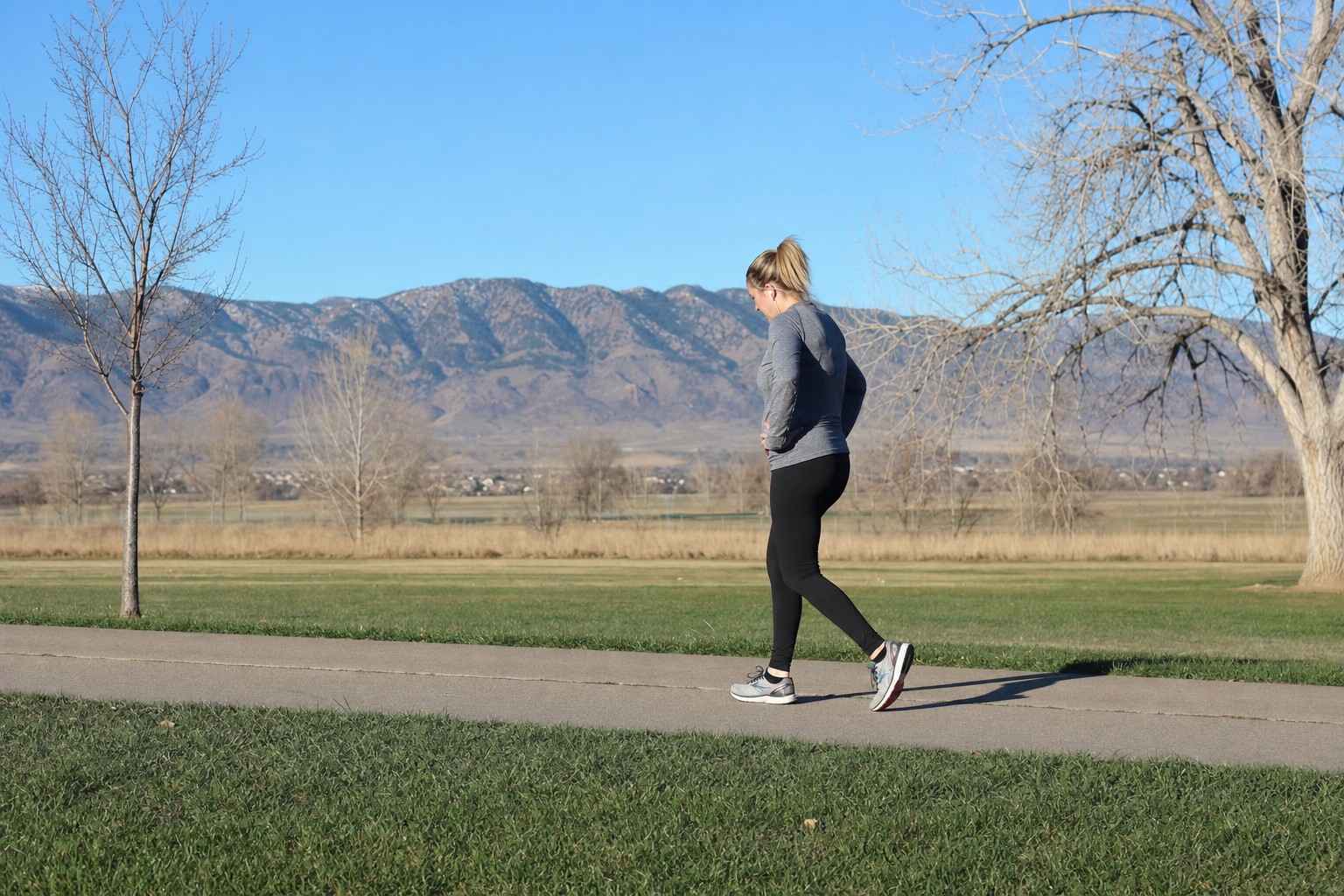 An ordinary beginner taking a walking break during a run on a flat paved park path on a calm Denver morning, hands on hips, catching their breath