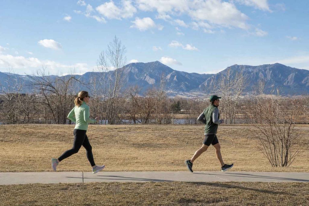 Two runners side-on at different paces on a city sidewalk on a cool March morning, both wearing touches of green