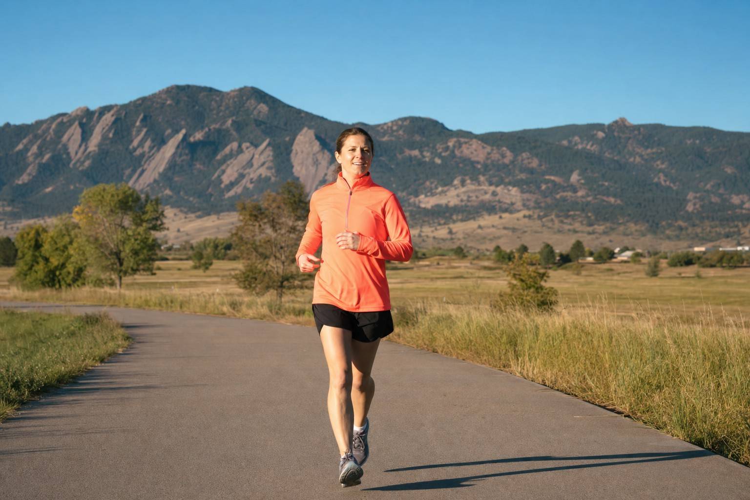 A single runner moving at a relaxed, easy, conversational effort along an open paved path on a clear Denver morning, looking comfortable