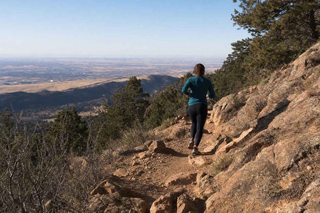 A single trail runner seen from behind heading up a rocky dirt singletrack trail into the foothills west of Denver