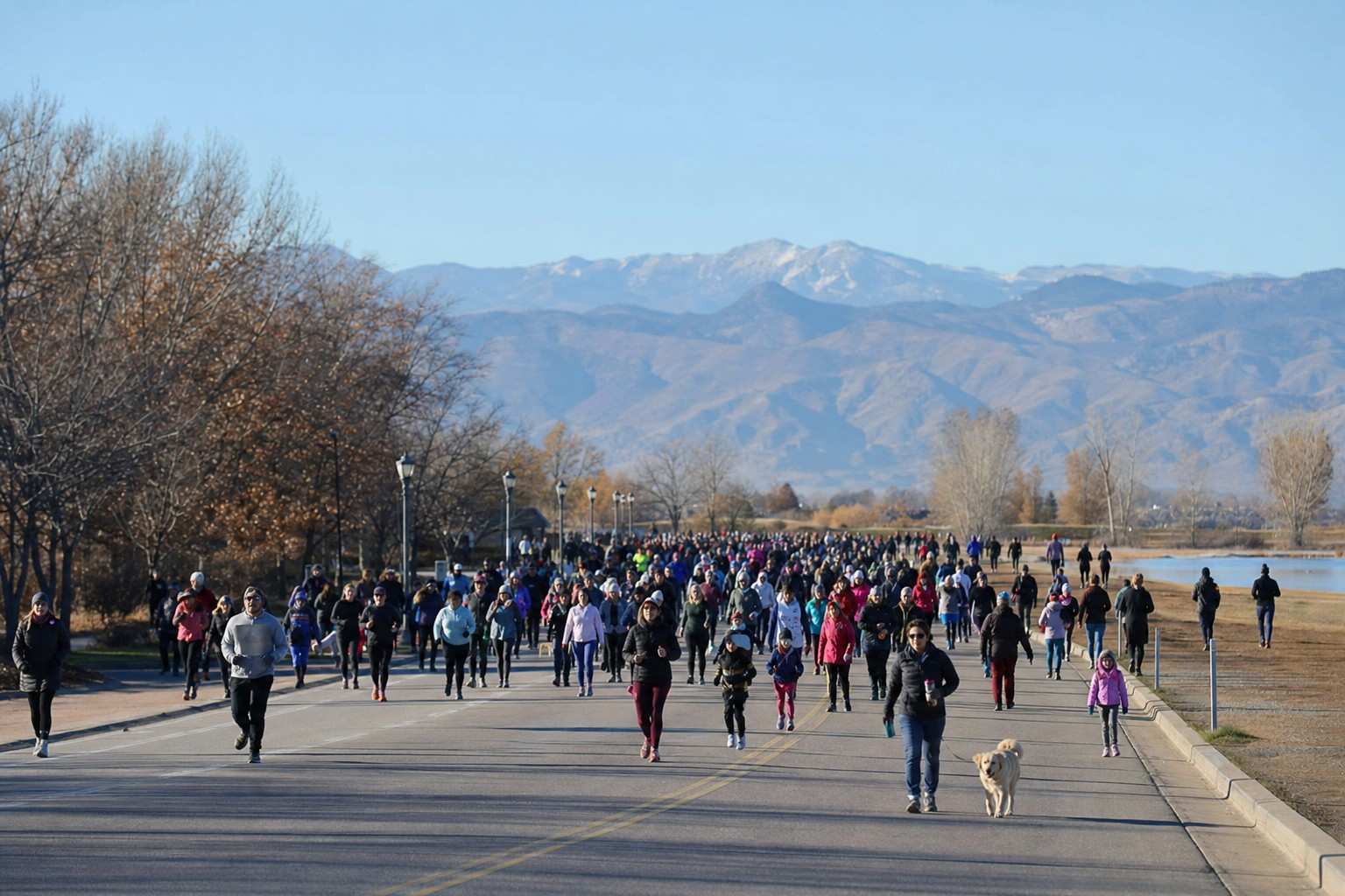 A festive crowd of walkers and runners in beanies and cold-weather layers filling a wide city street on a chilly late-November morning