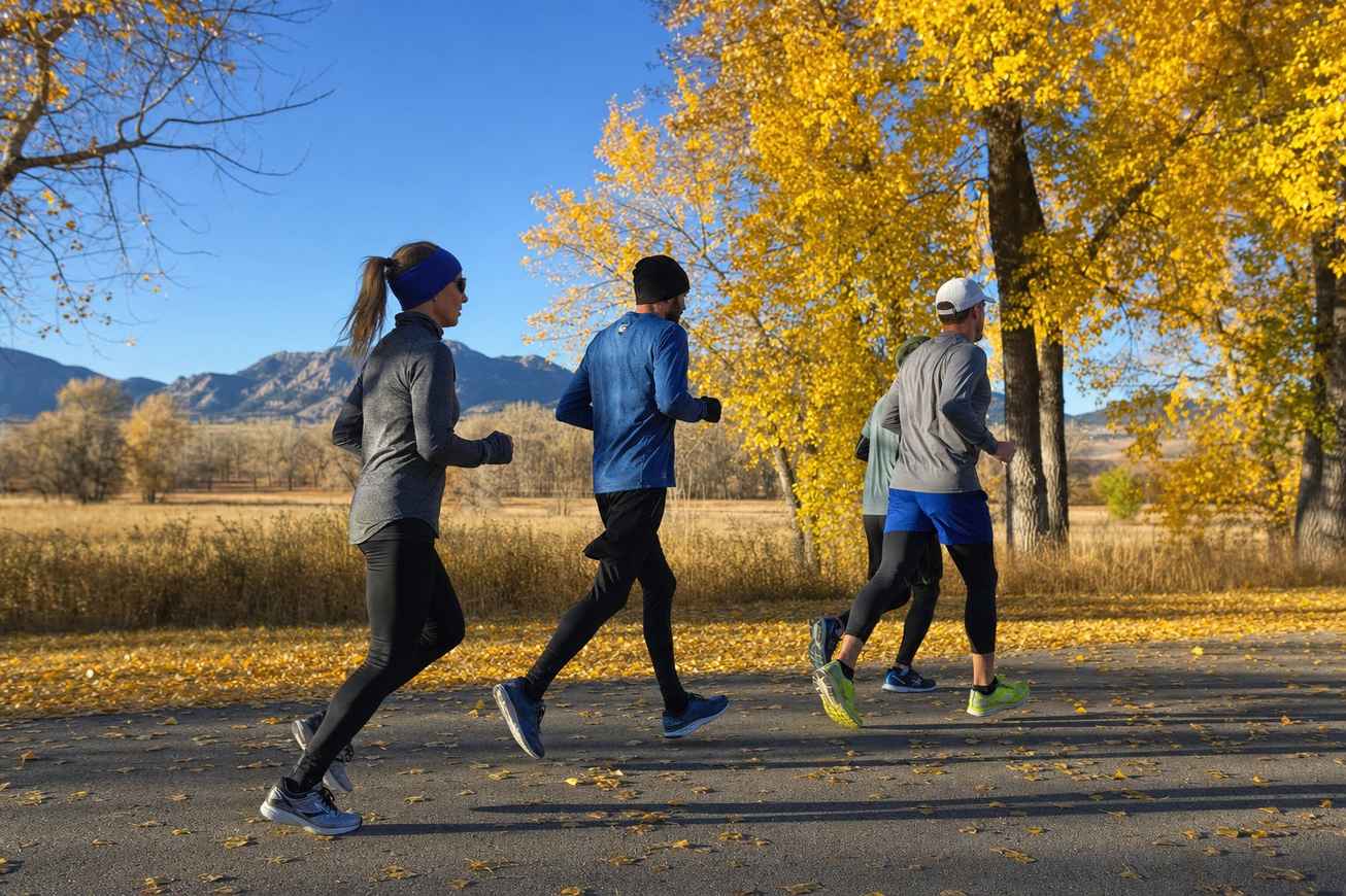 A small group of everyday runners moving along a park road lined with golden fall trees on a crisp Denver morning