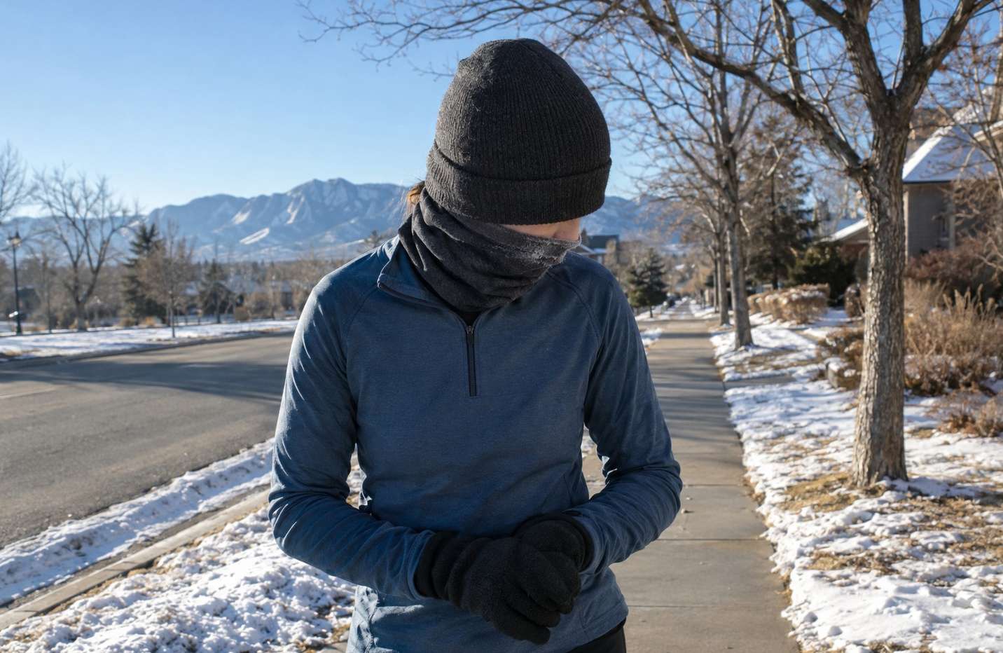 A runner on a frosty Denver sidewalk in gloves, a knit hat and a neck gaiter pulled up, frost on the fabric around the mouth