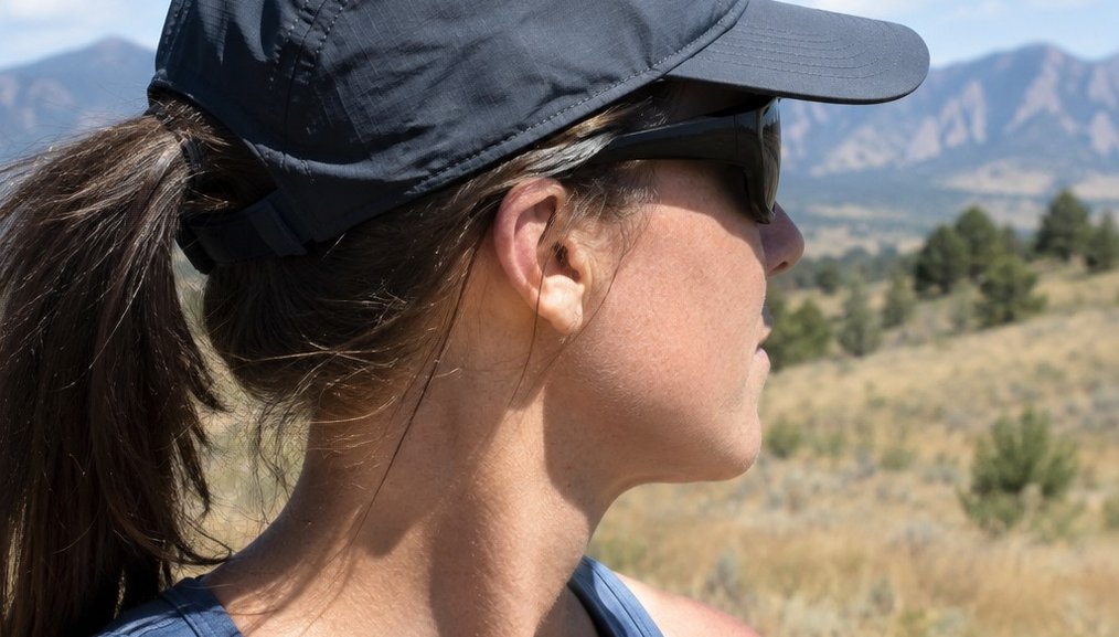 A brimmed cap and sunglasses on a runner at midday, the brim throwing a hard shadow across the face